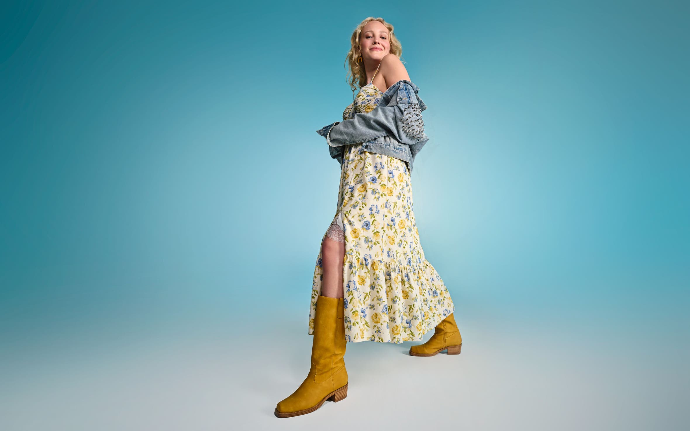 A woman wearing a floral-print maxi dress with a denim jacket and yellow boots.