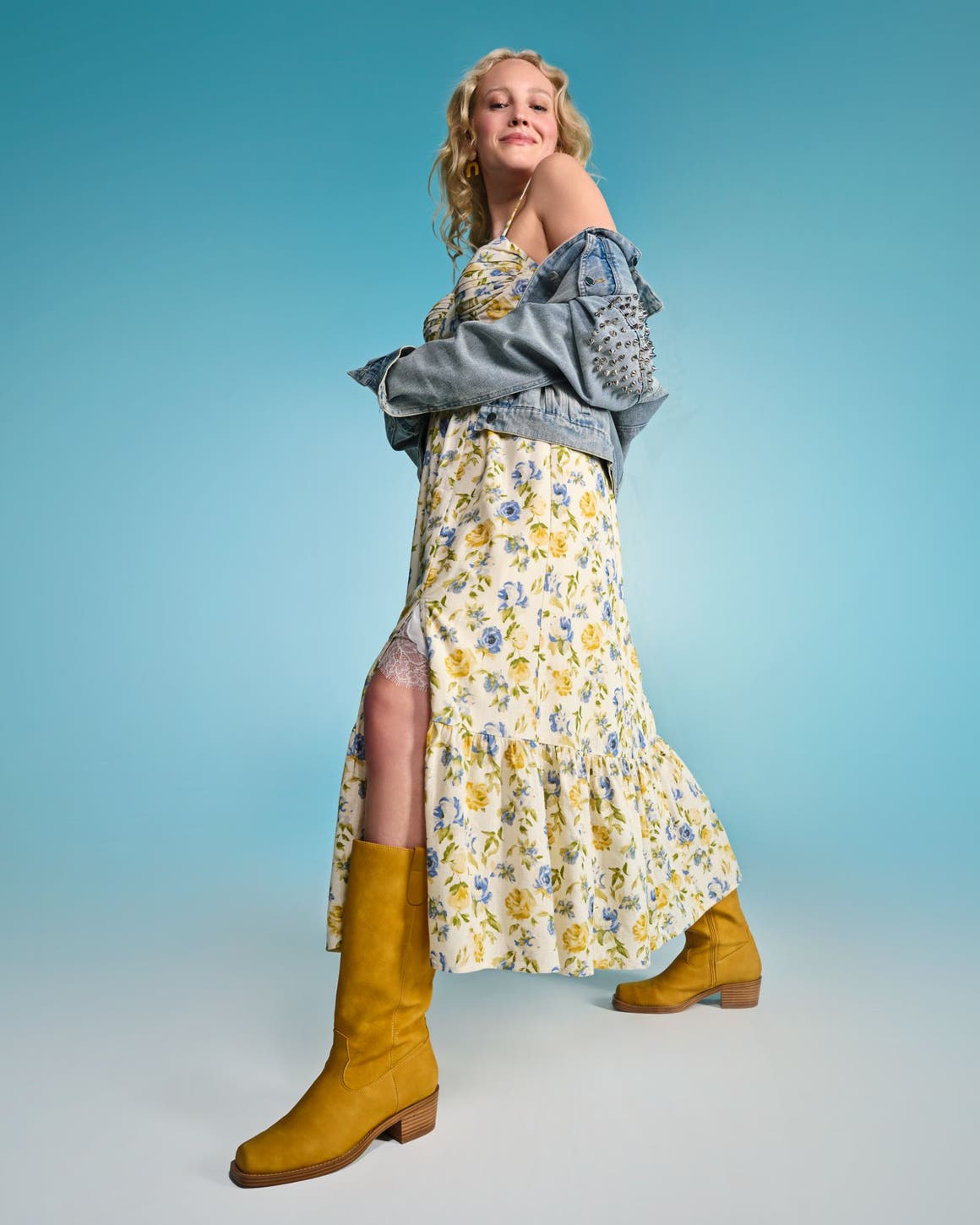 A woman wearing a floral-print maxi dress with a denim jacket and yellow boots.
