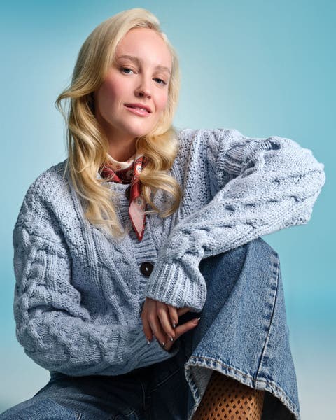 Woman wearing a light blue cable‑knit cardigan and blue jeans.