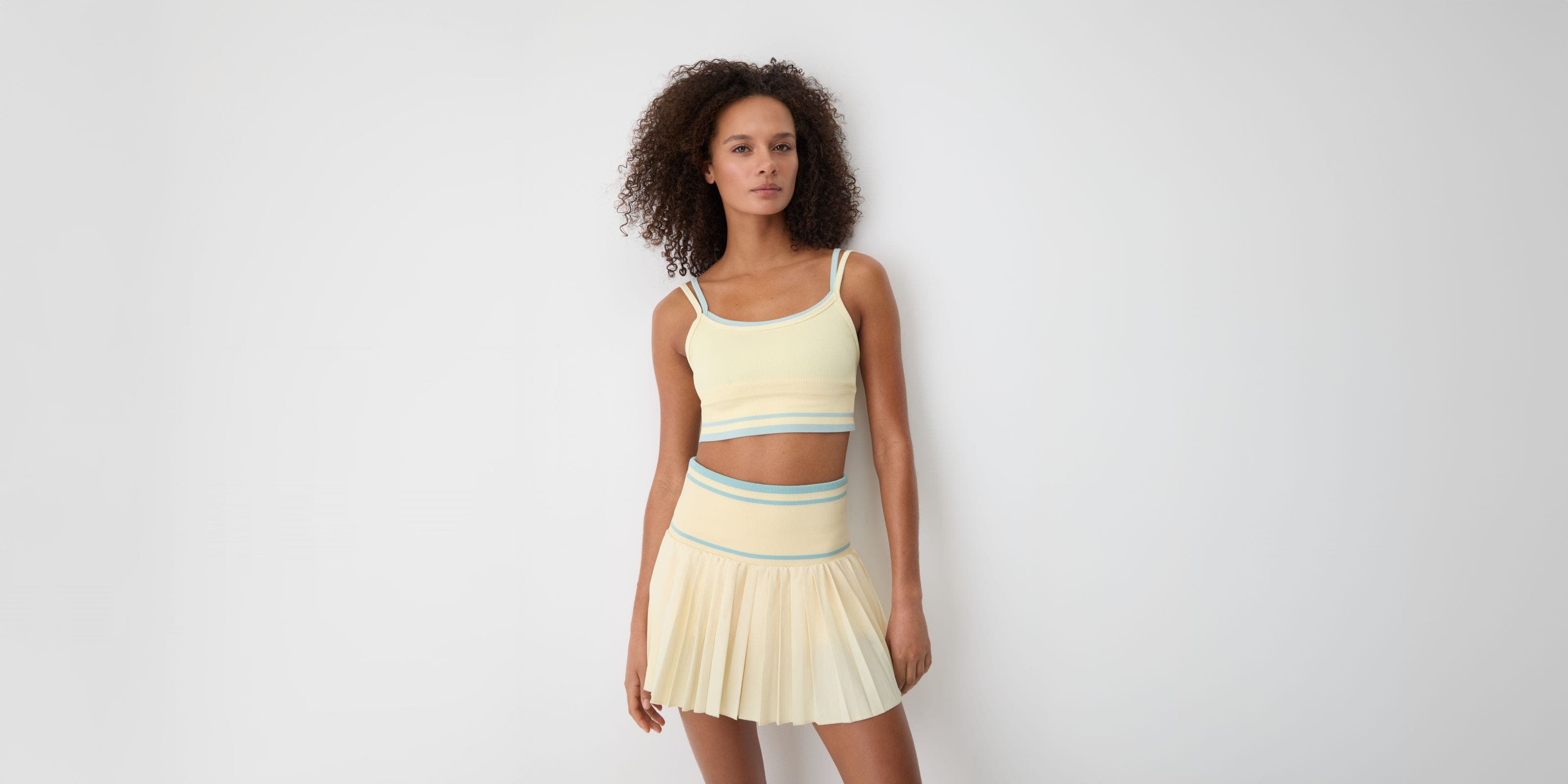 A woman wearing a yellow matching tennis skirt and sports bra.