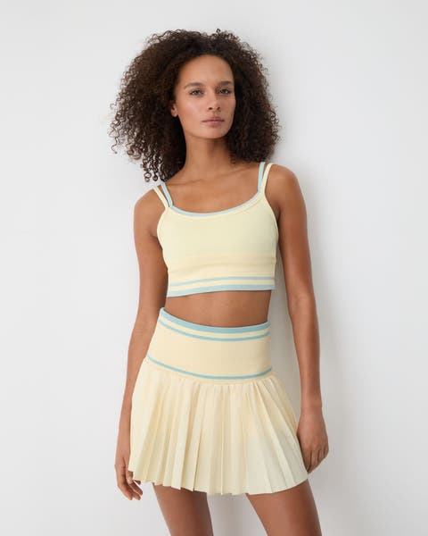 A woman wearing a yellow matching tennis skirt and sports bra.