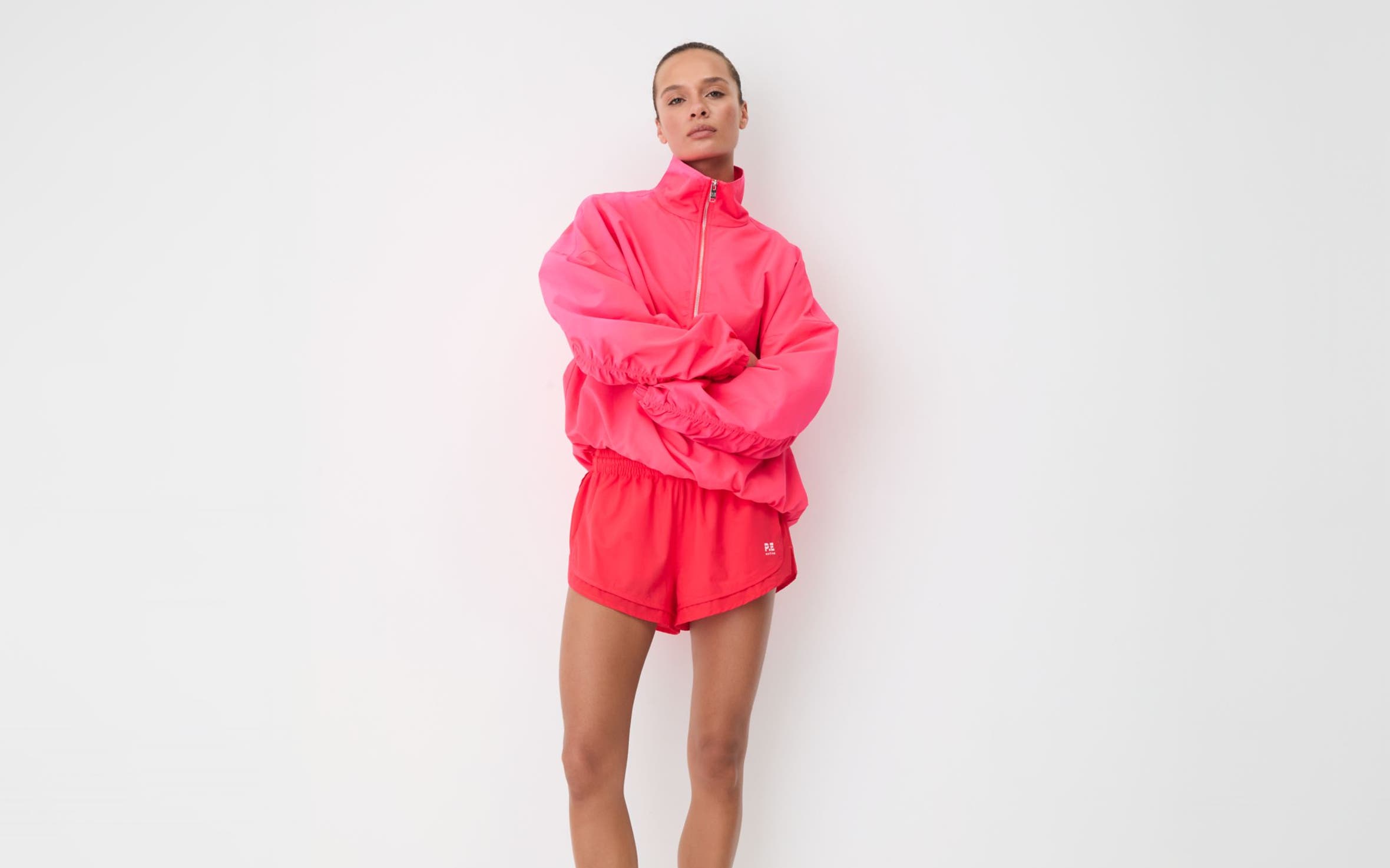Woman in a pink half-zip pullover and pink runner shorts with white crew socks and silver sneakers.