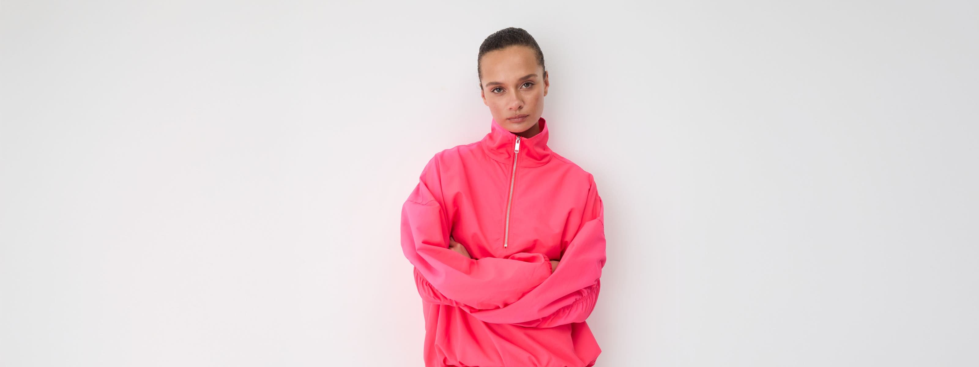 Woman in a pink half-zip pullover and pink runner shorts with white crew socks and silver sneakers.