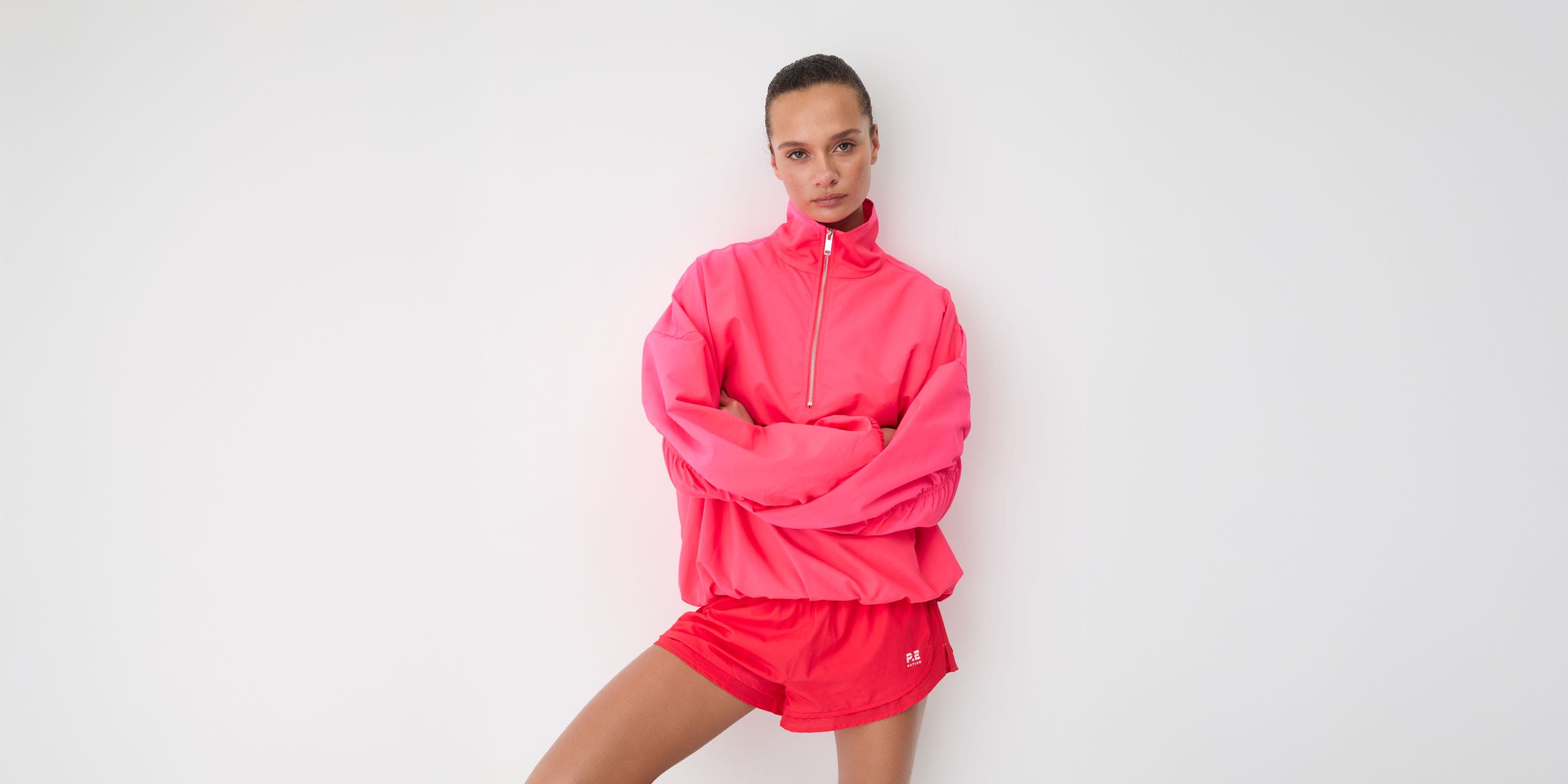 Woman in a pink half-zip pullover and pink runner shorts with white crew socks and silver sneakers.