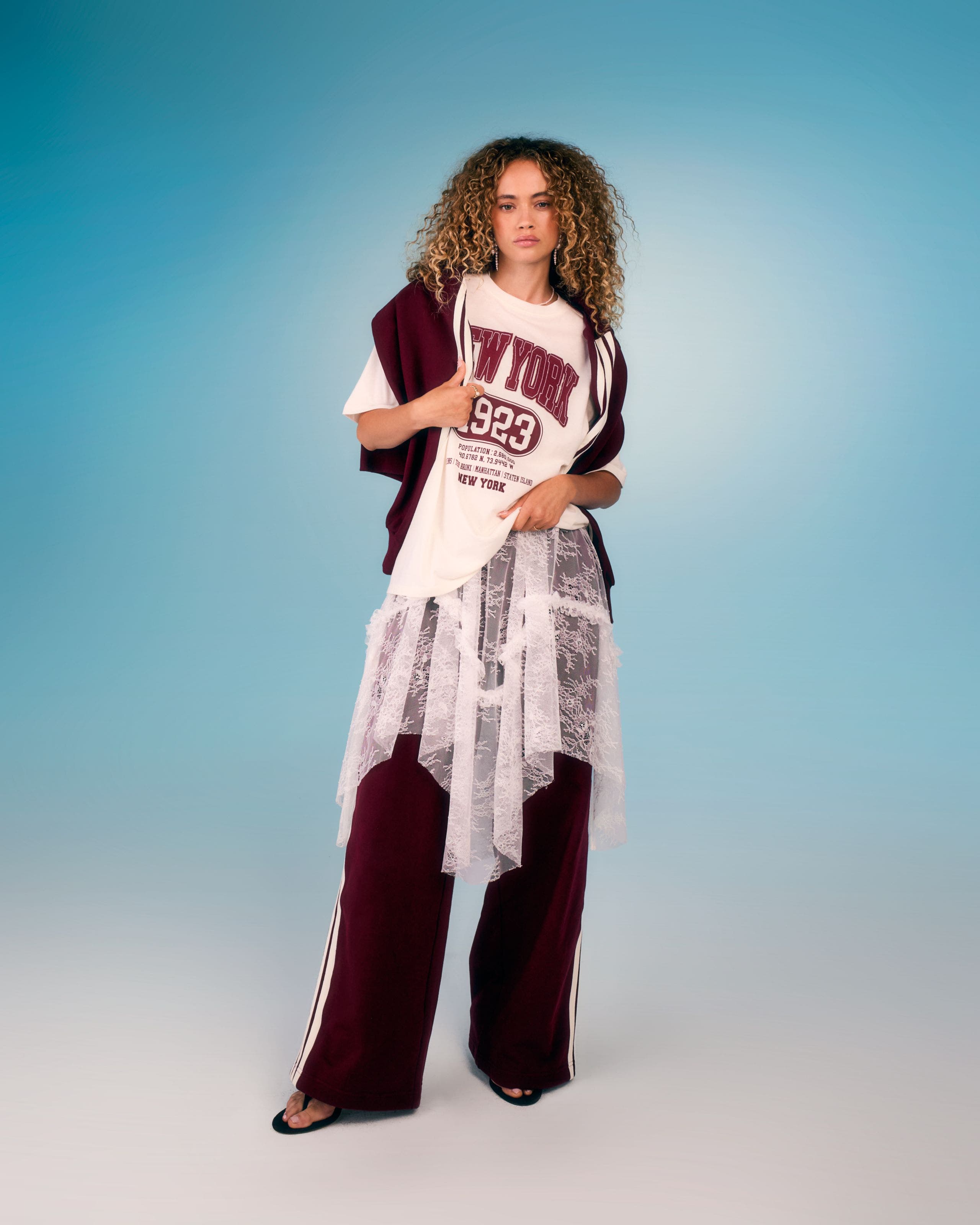Model wearing a graphic tee layered over a lace top with burgundy track pants.