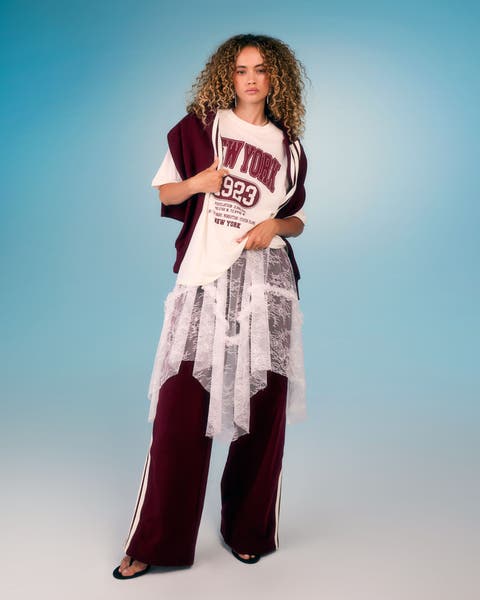 Model wearing a graphic tee layered over a lace top with burgundy track pants.