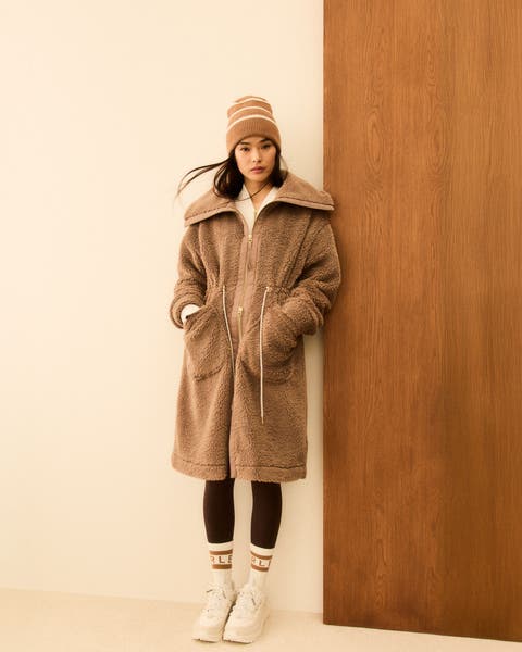 Woman wearing a zip-up fleece coat, leggings, crew socks, sneakers and a beanie.