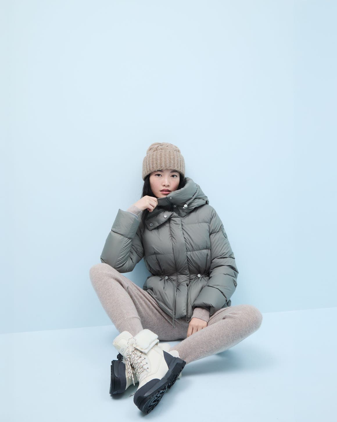 Woman wearing a puffer, boots, cashmere hoodie, jogger pants and beanie.