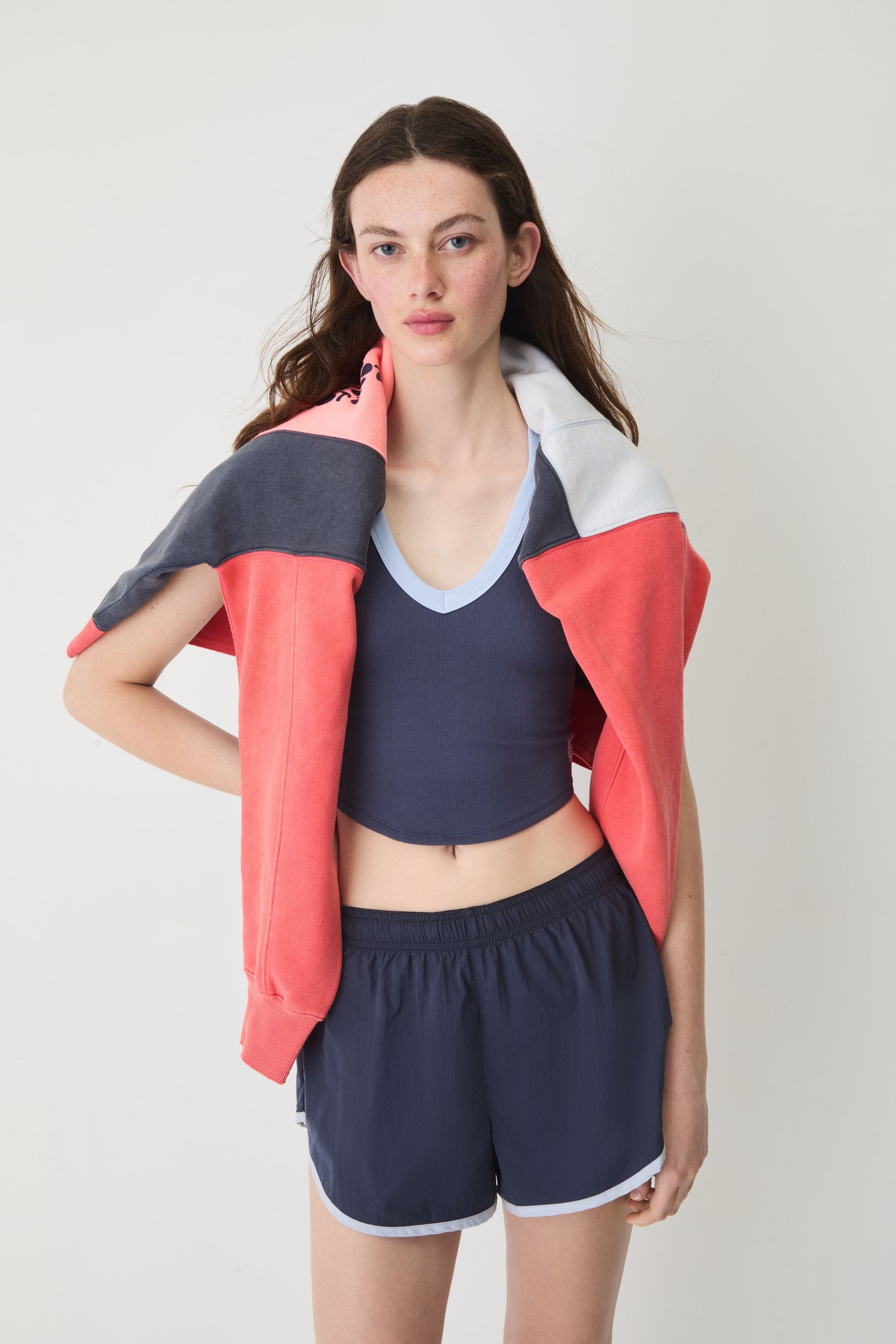 A woman wearing a navy tank and shorts with a sweatshirt over her shoulders.
