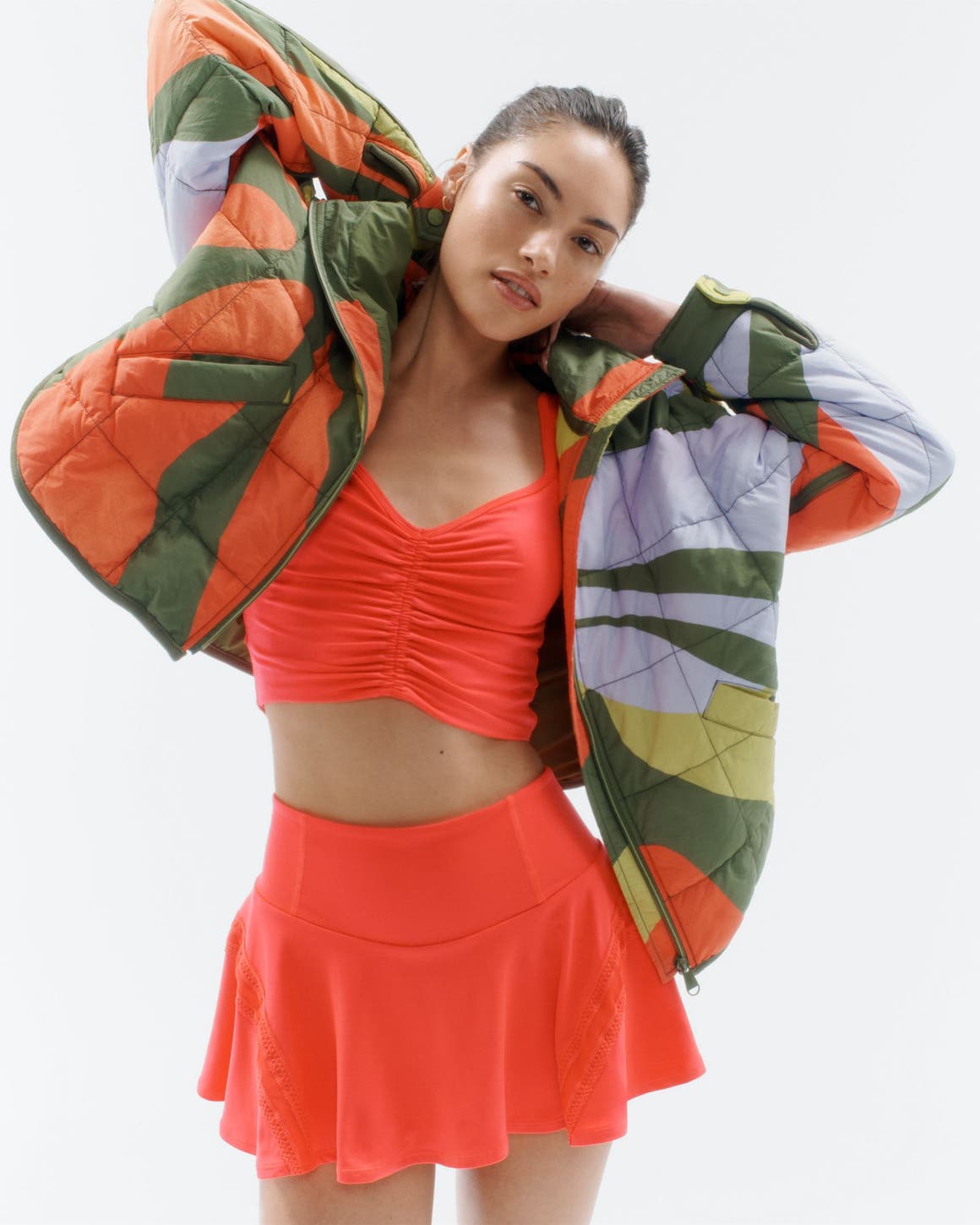 A woman wearing an activewear tank and skirt with a quilted jacket.