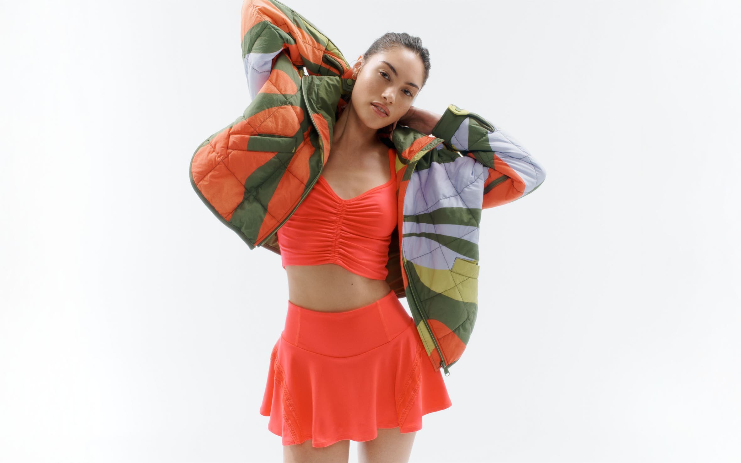 A woman wearing an activewear tank and skirt with a quilted jacket.