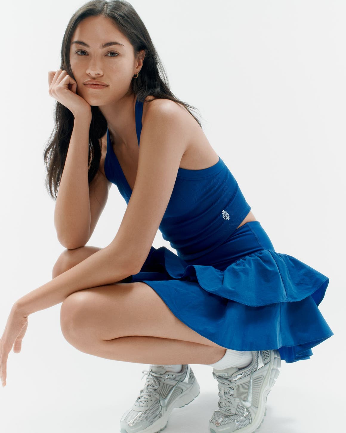 A woman wearing an activewear tank, skirt and sneakers.