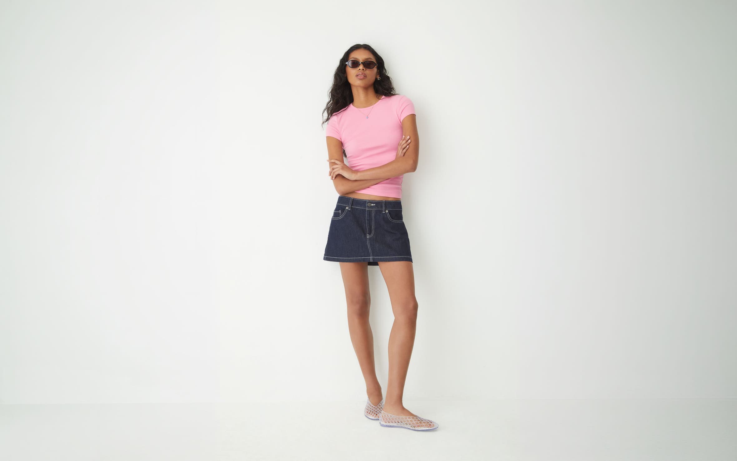 A woman wearing a pink T-shirt and denim skirt.