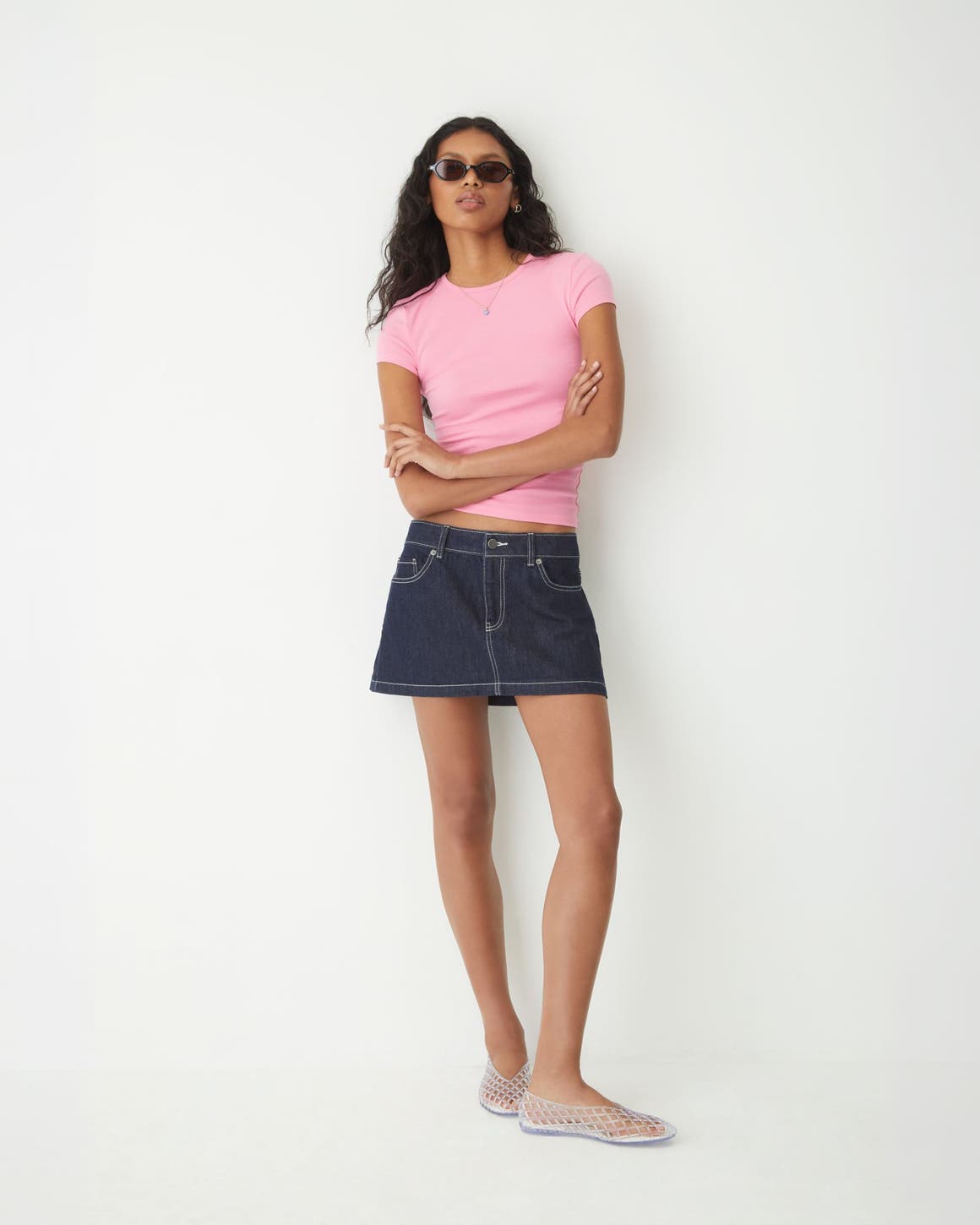A woman wearing a pink T-shirt and denim skirt.
