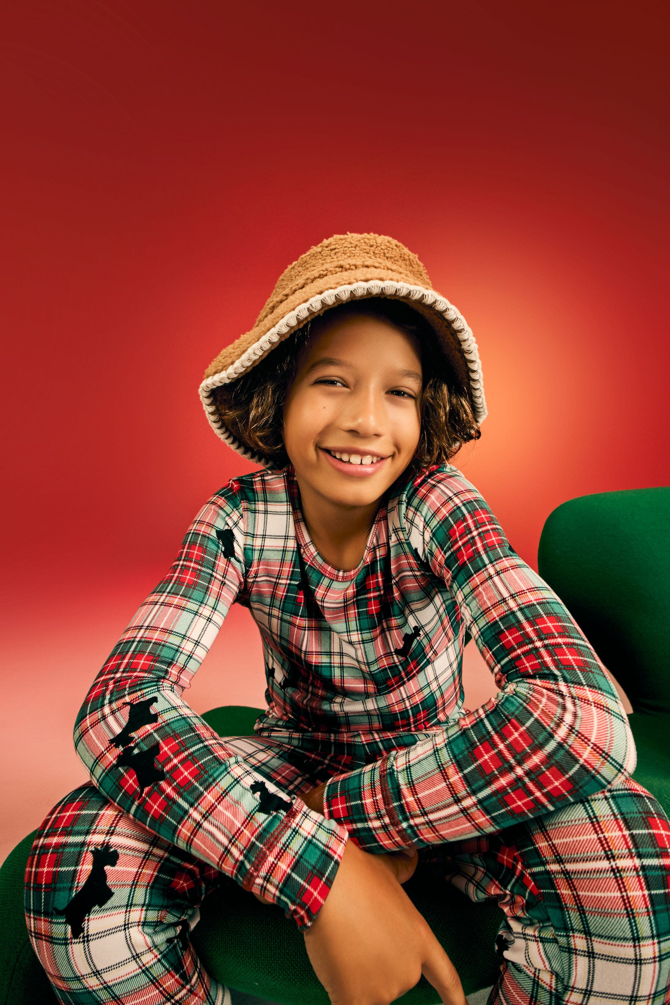 Child model wearing a red and green plaid holiday pajama set with scotty dog print and a tan bucket hat.