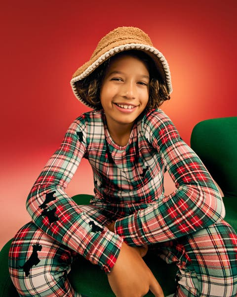 Child model wearing a red and green plaid holiday pajama set with scotty dog print and a tan bucket hat.