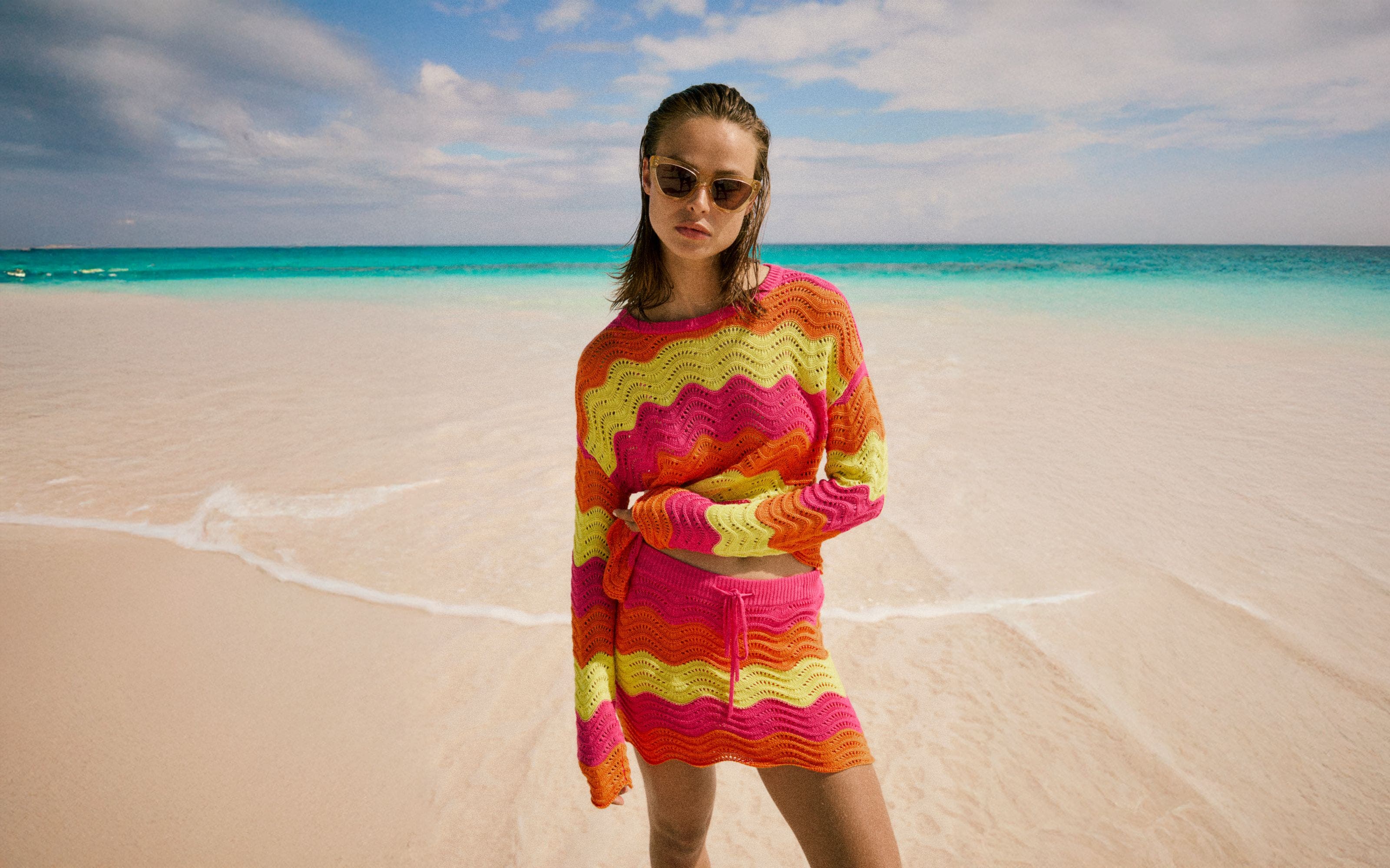 A woman wearing a bright zig-zag striped crochet top and matching skirt.