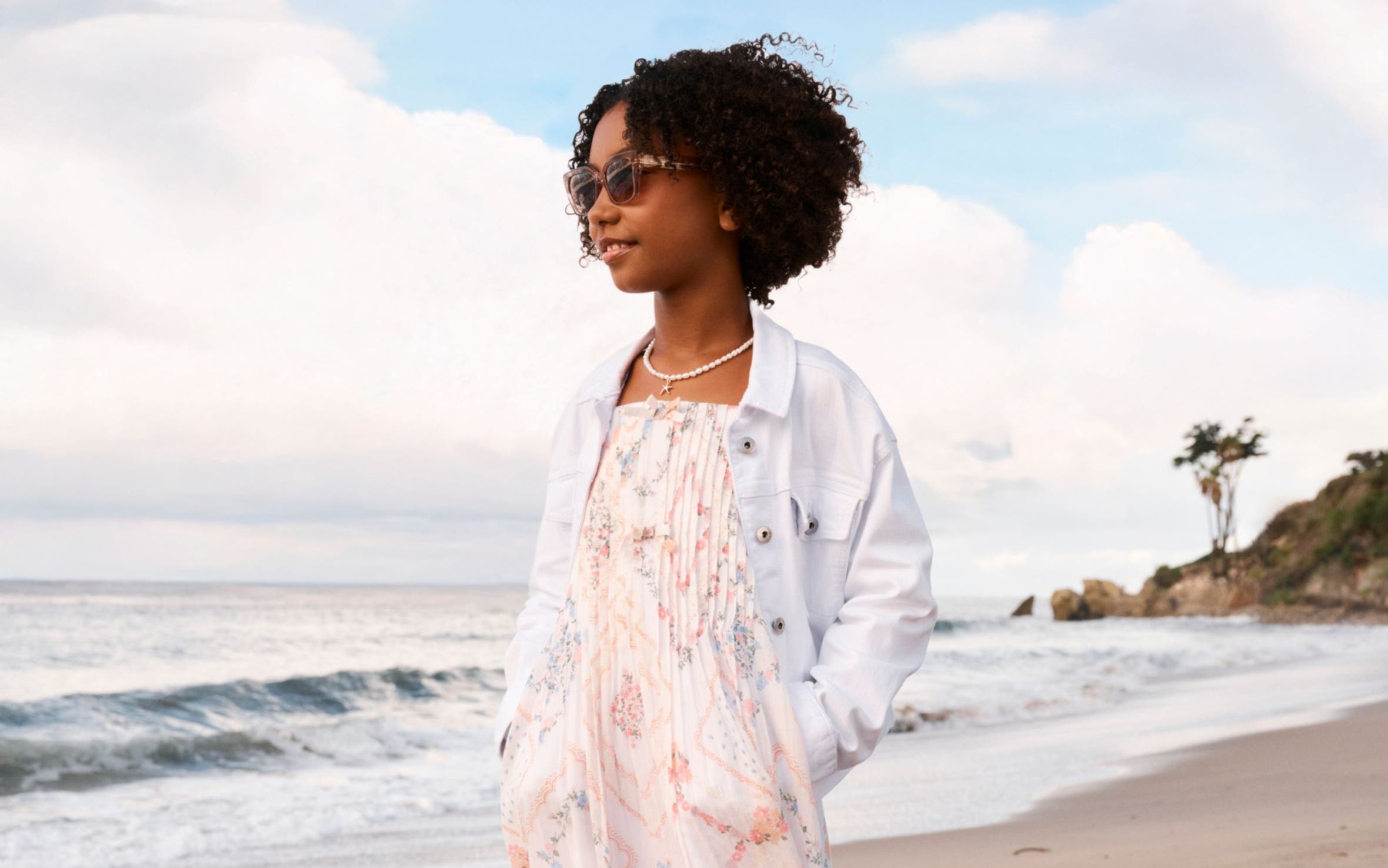 A tween girl wearing a sundress and a white denim jacket.