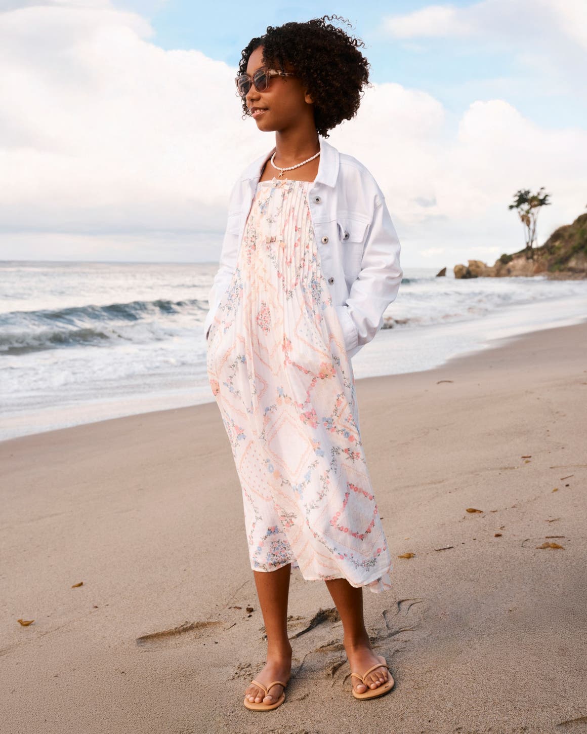 A tween girl wearing a sundress and a white denim jacket.
