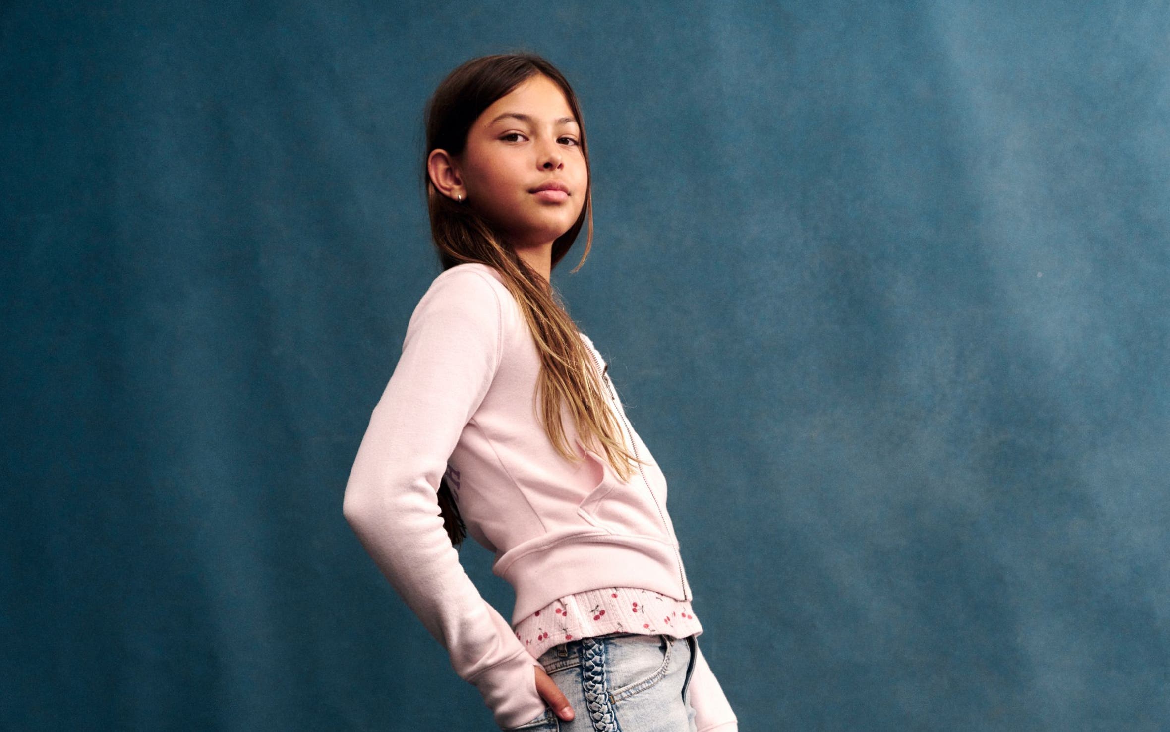A girl posing in a pink long-sleeve top with a floral trim hem and light wash jeans.