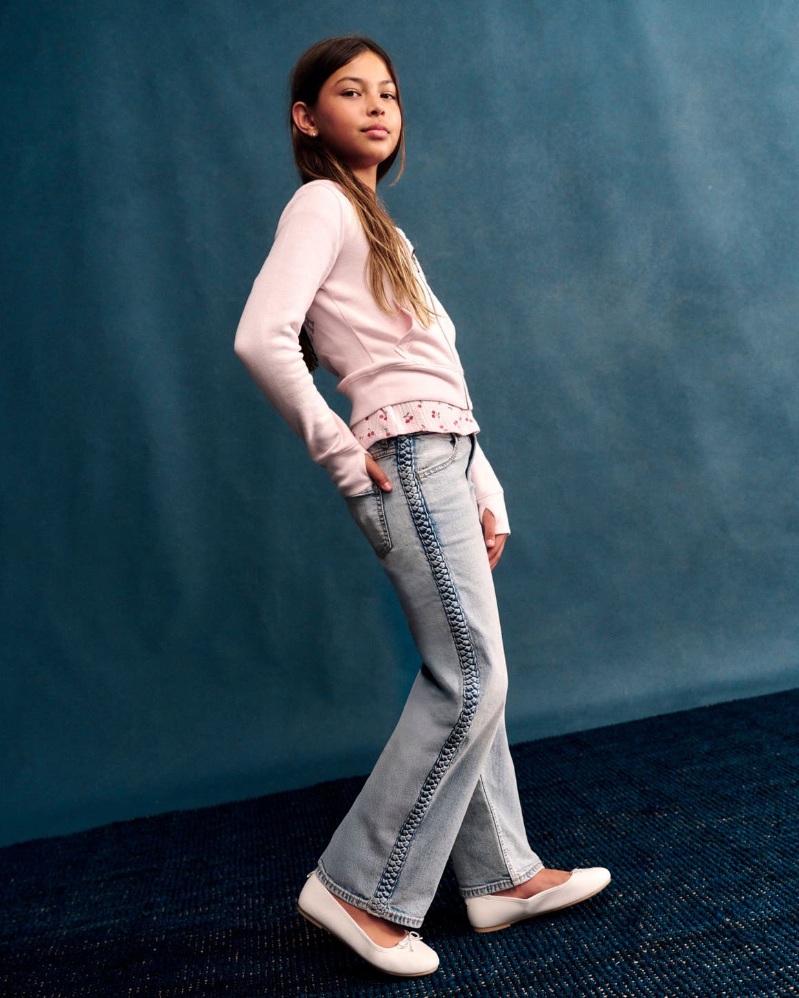 A girl posing in a pink long-sleeve top with a floral trim hem and light wash jeans.