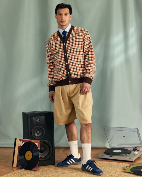 A man wearing a plaid cardigan over a button-up shirt and tie with shorts and sneakers.