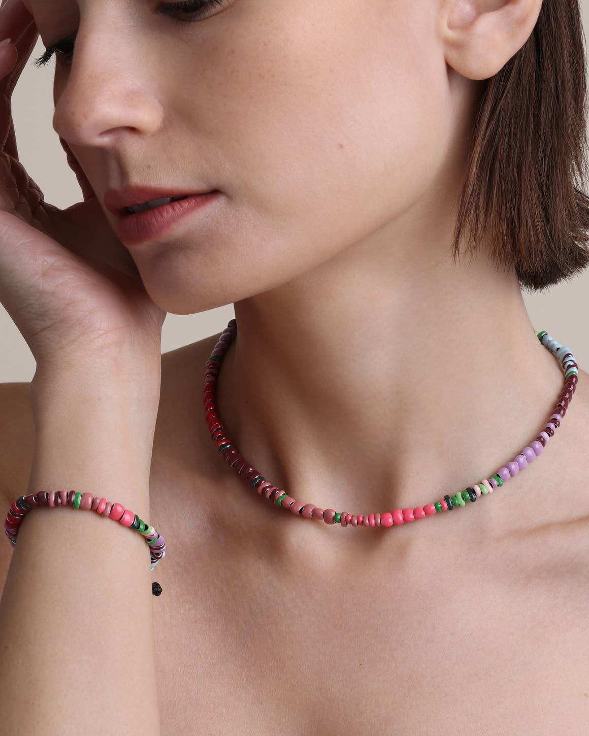 A woman wearing a necklace and bracelet made of multicolored beads.