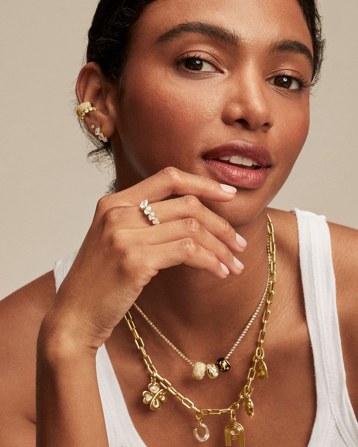 A woman wearing earrings, a ring and charm necklaces. 
