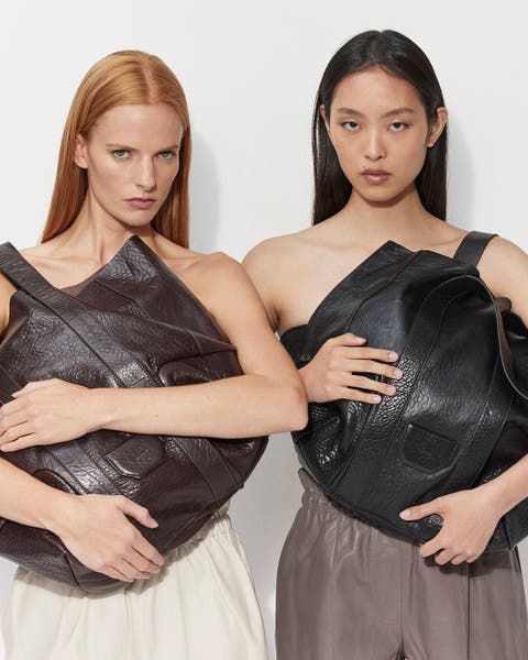 Two women holding leather Allsaints bags.