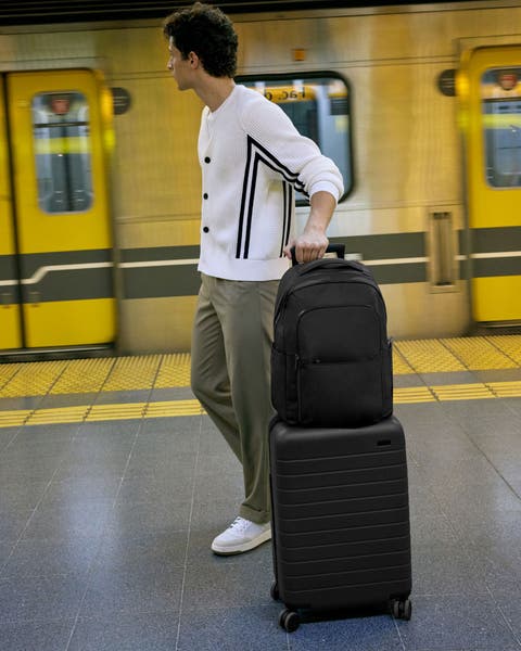 A man rolling a suitcase and backpack.