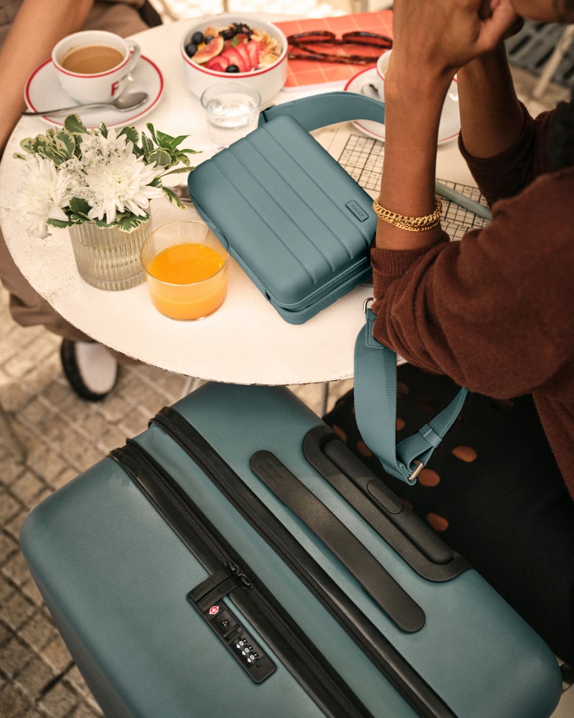 A couple sitting at a table with a suitcase and travel bag. 
