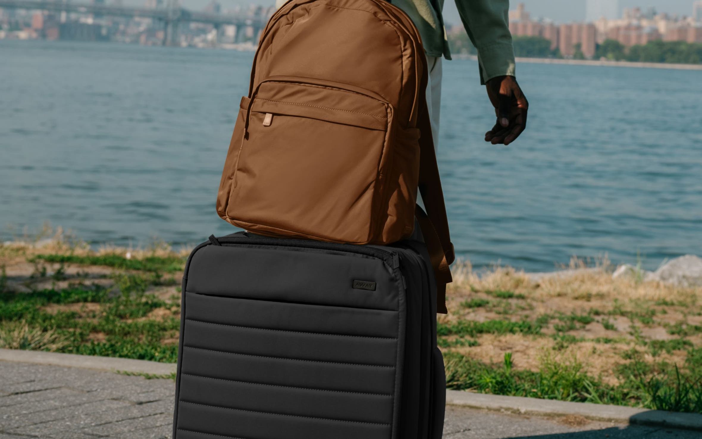 A man with a brown backpack and black roller suitcase.	