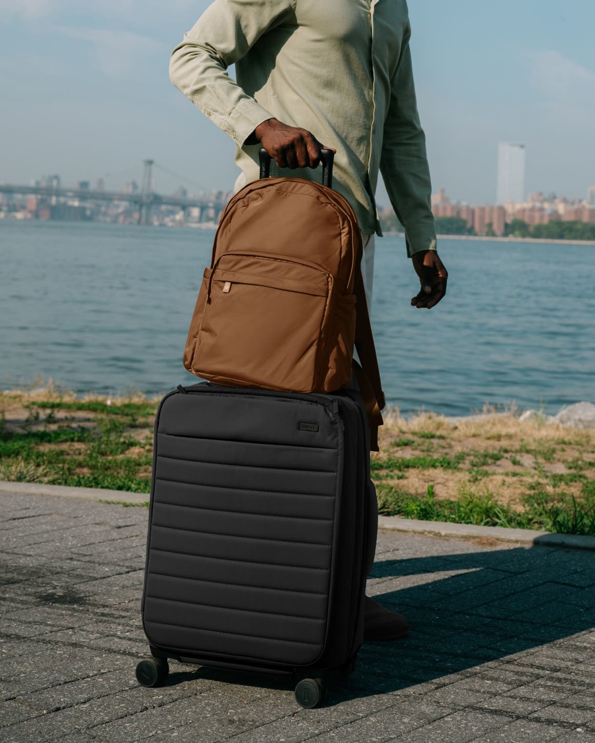 A man with a brown backpack and black roller suitcase.	