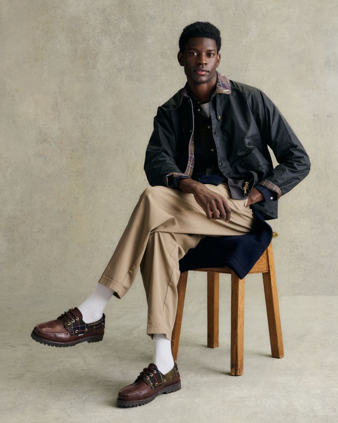 A man in Barbour Jacket, tan pants, and brown shoes sitting down.