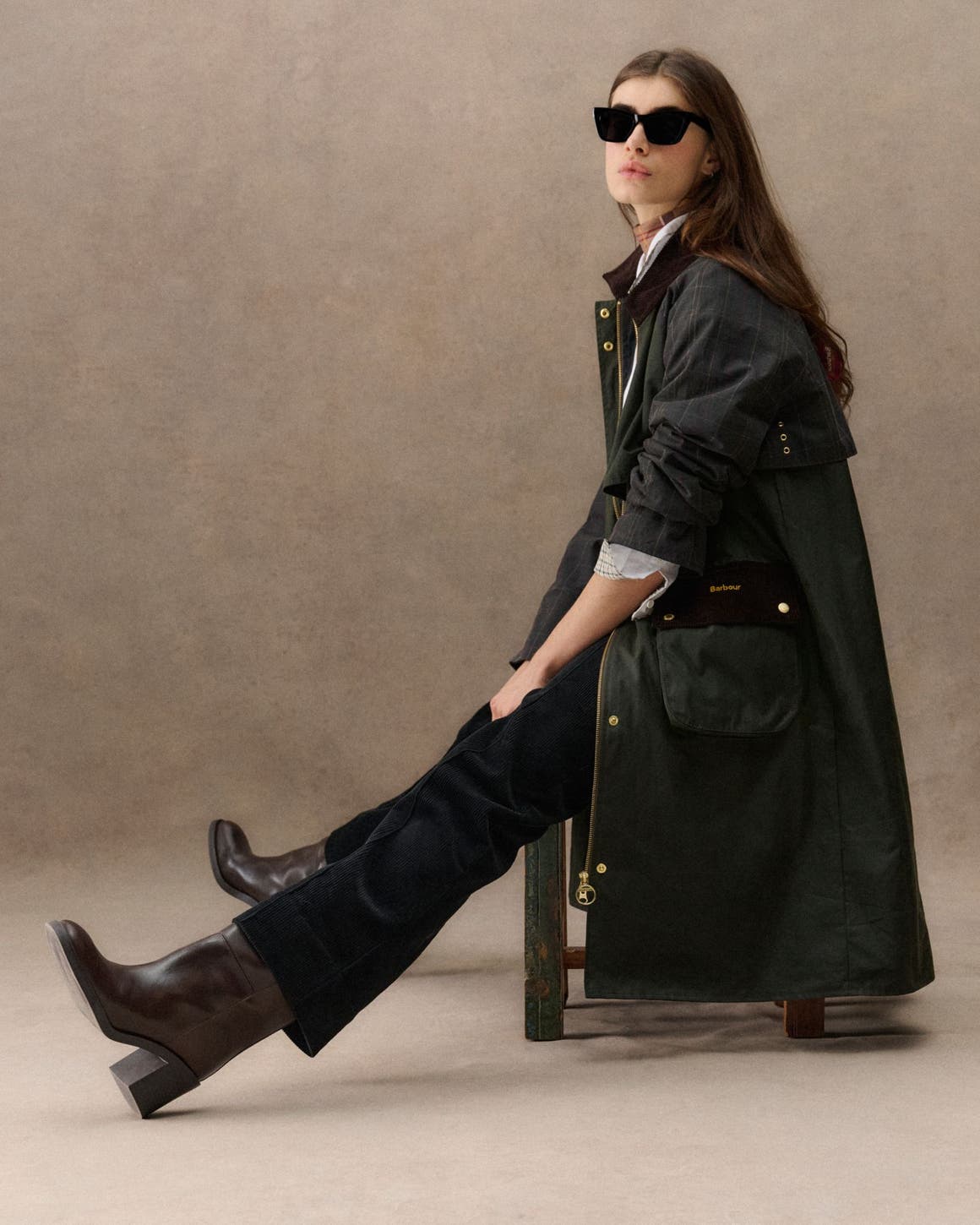 A woman sitting in a green Barbour raincoat.