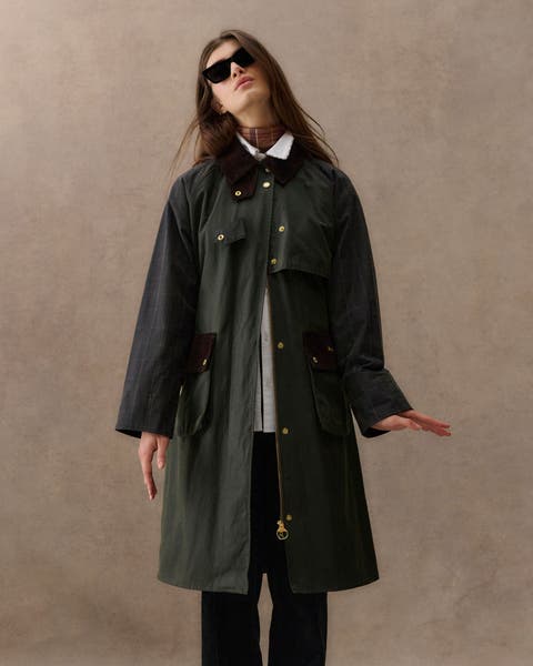 A woman wearing a long green Barbour rain coat. 