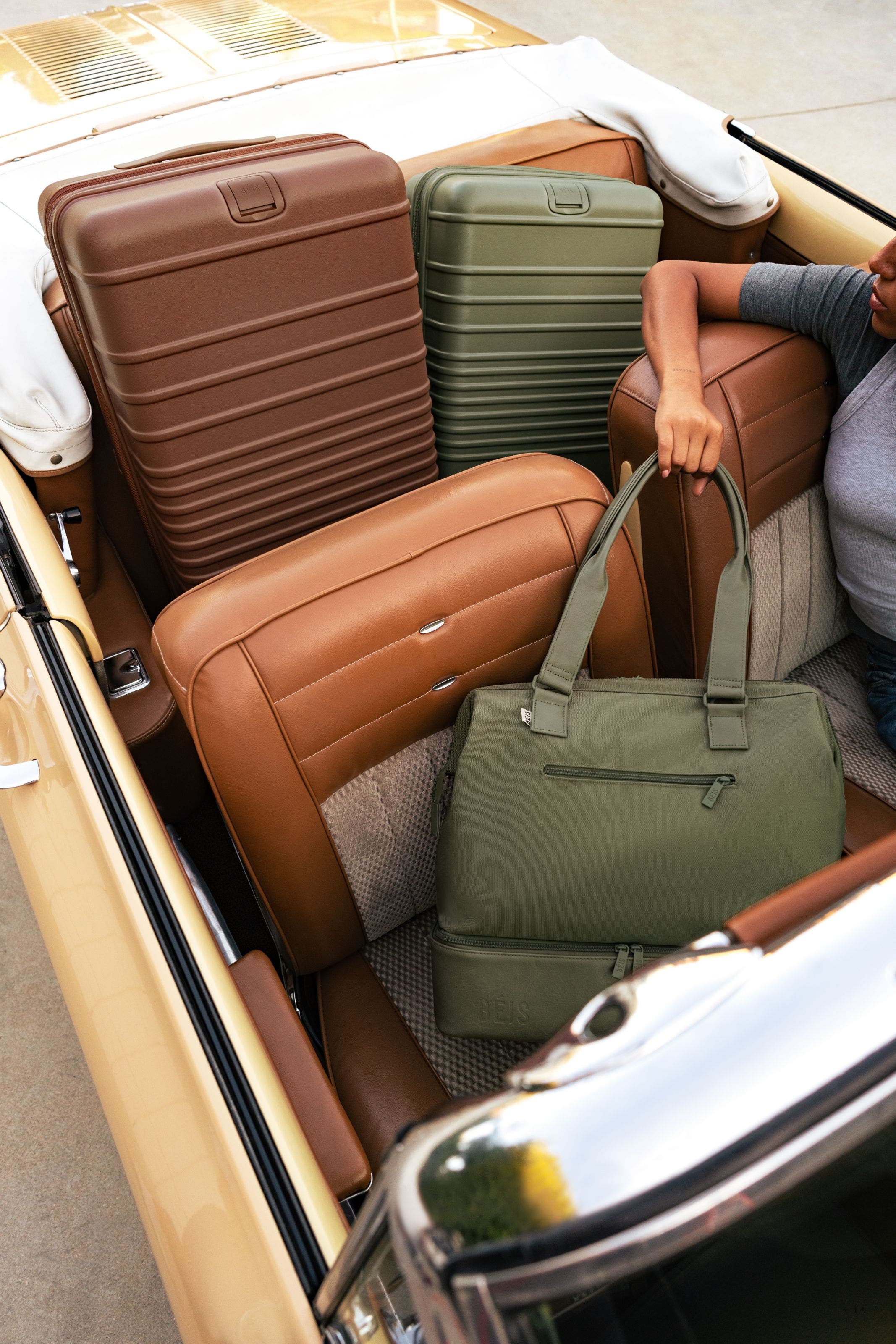 Woman holding a green tote in a car with luggage in the back seat.