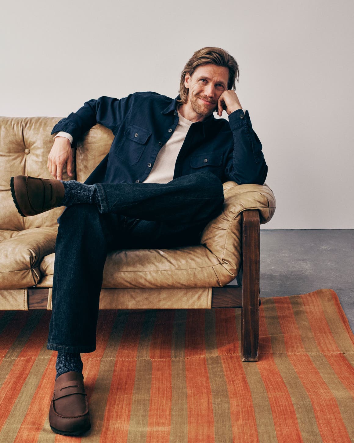 A man wearing a button-up shirt over a tee with jeans and loafers.