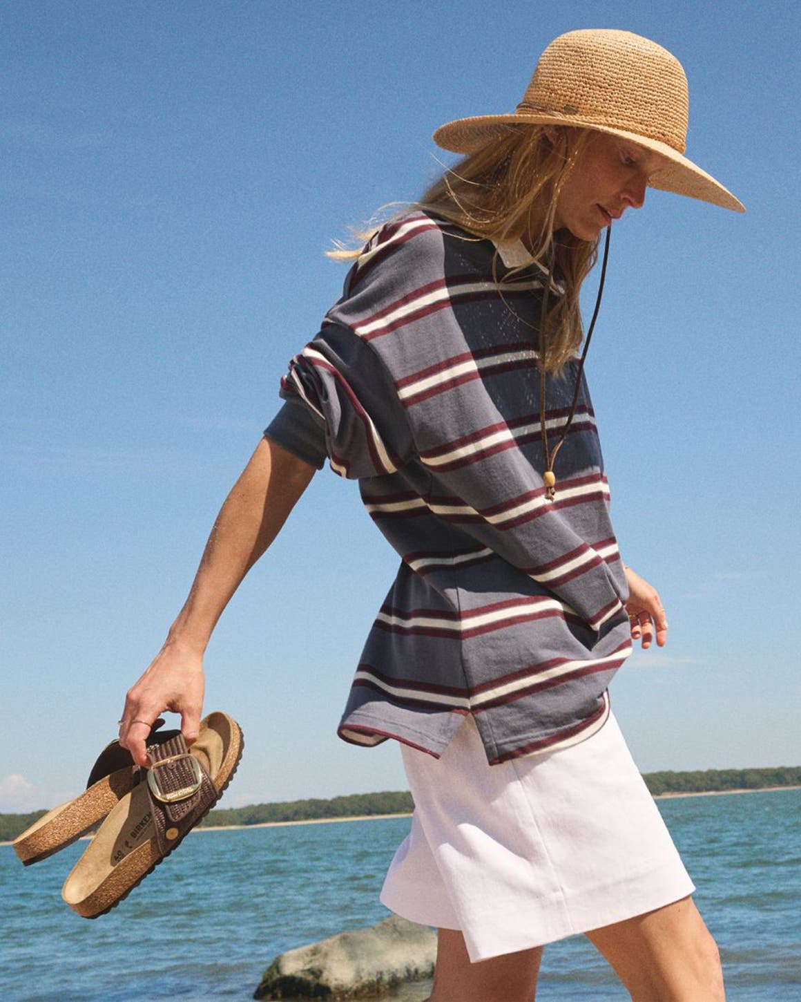 Woman walking on the beach holding Birkenstock sandals.
