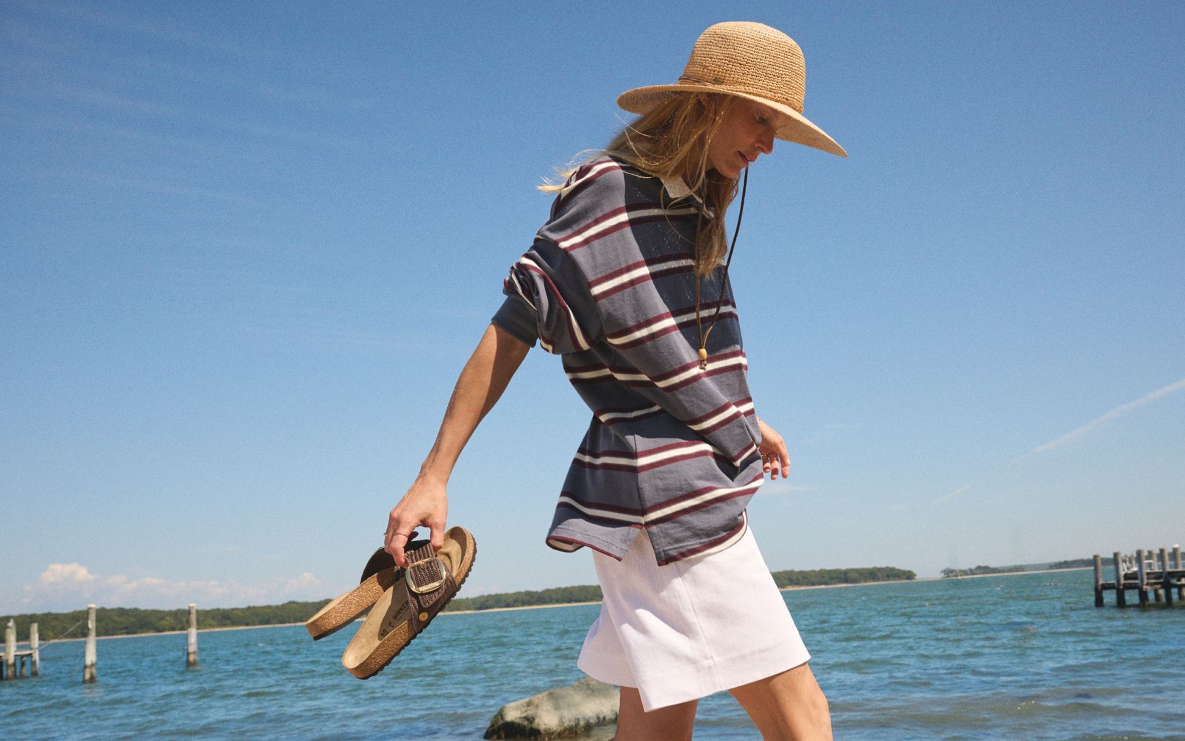 Woman walking on the beach holding Birkenstock sandals.