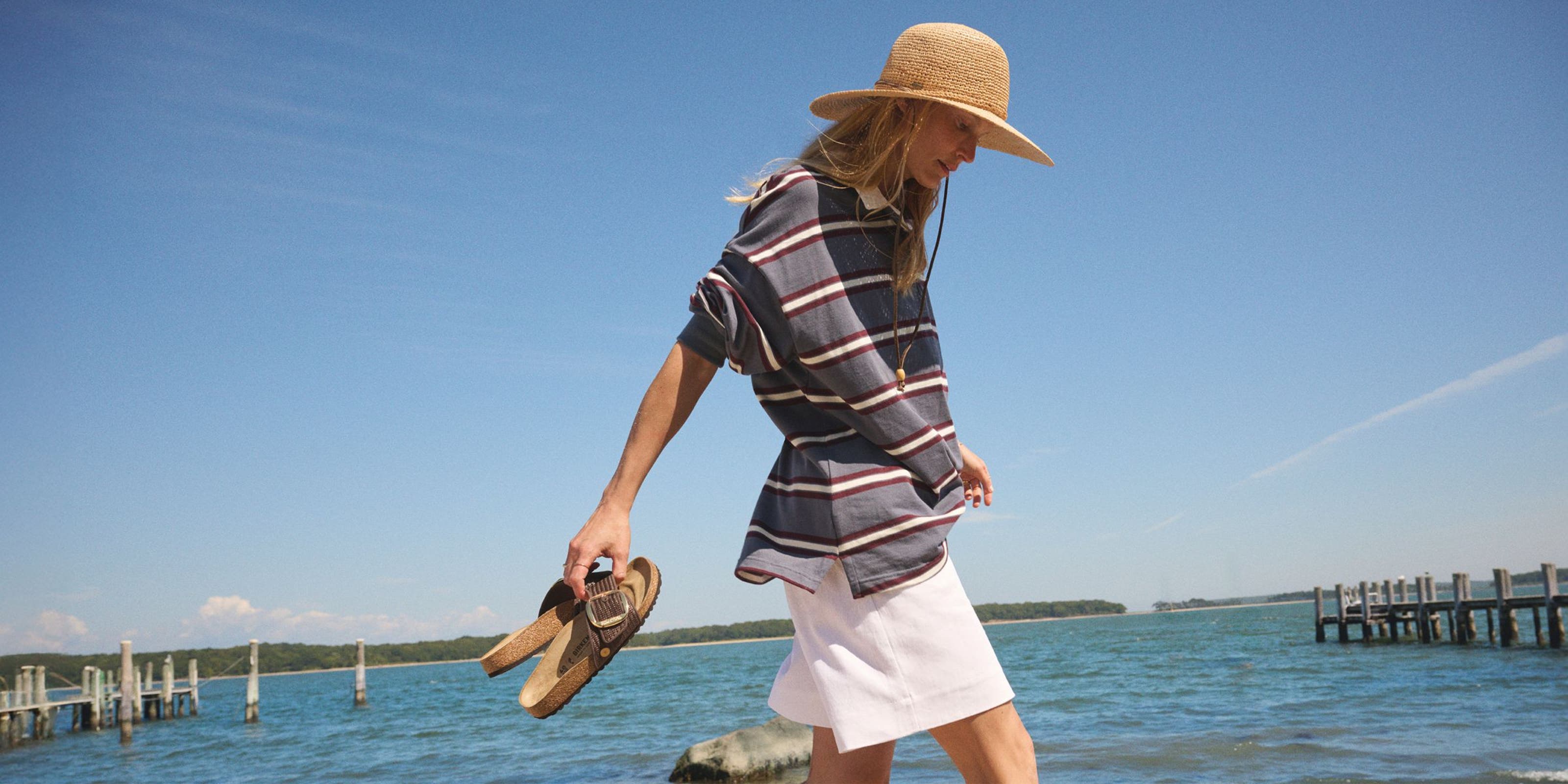 Woman walking on the beach holding Birkenstock sandals.