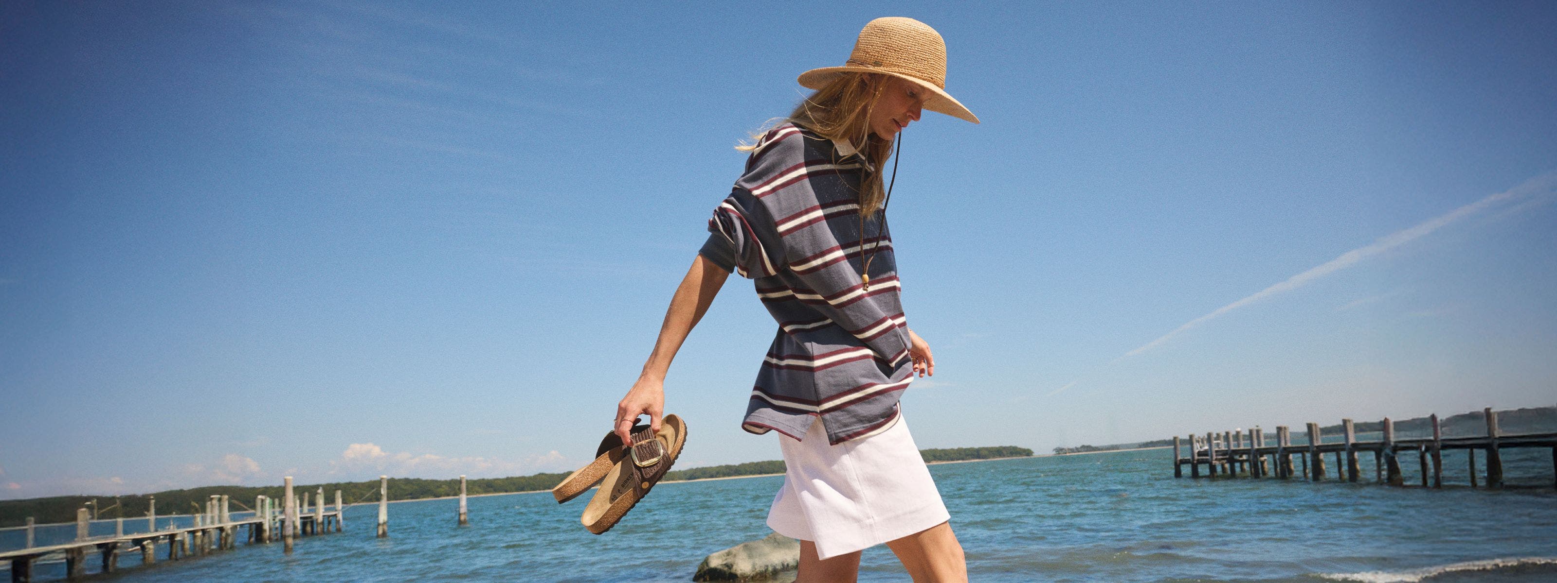 Woman walking on the beach holding Birkenstock sandals.