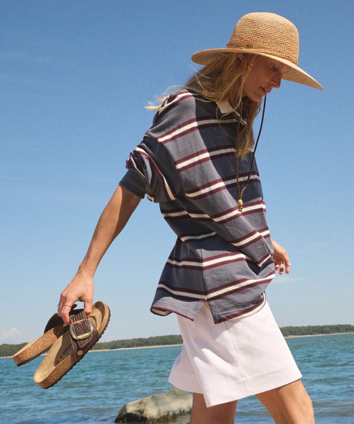 Woman walking on the beach holding Birkenstock sandals.