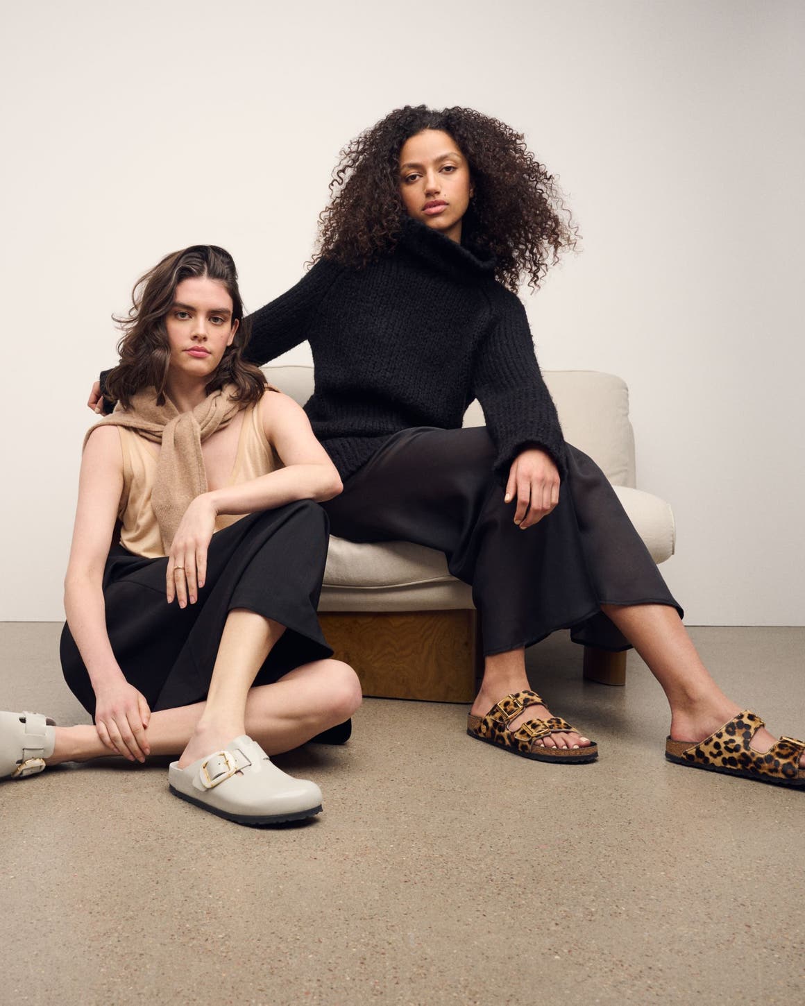 Two women seated wearing Birkenstock Boston clogs and Arizona sandals in black and leopard pony hair styles.