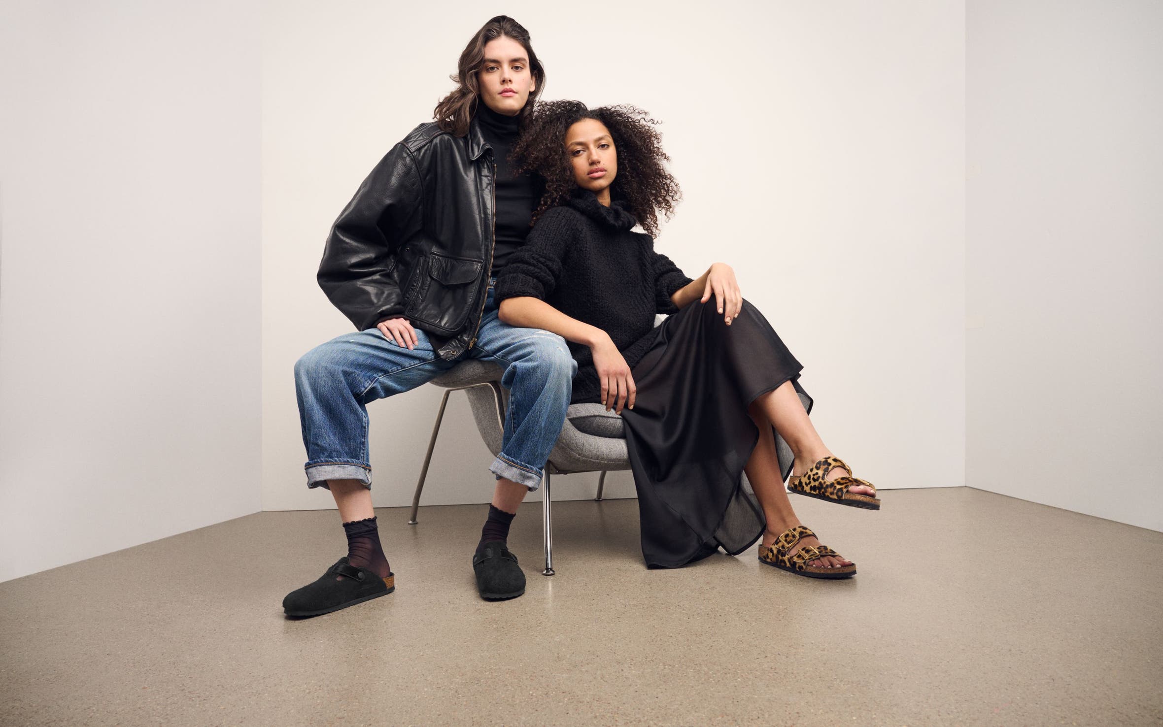 Two women seated wearing Birkenstock Boston clogs and Arizona sandals in black and leopard pony hair styles.