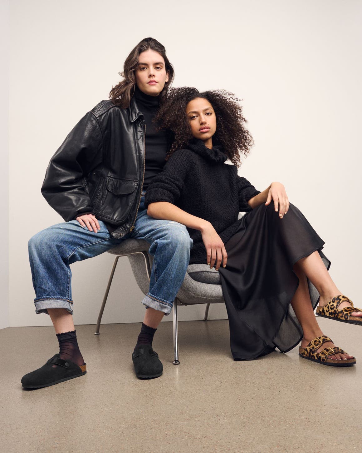 Two women seated wearing Birkenstock Boston clogs and Arizona sandals in black and leopard pony hair styles.