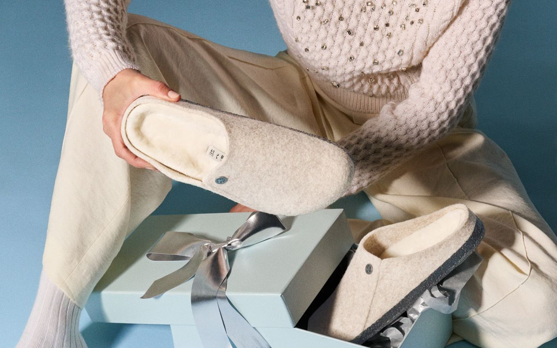 A woman opening a gift box that contains Birkenstock slippers.