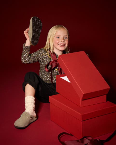 Little girl opening a red gift box with Birkenstock clogs