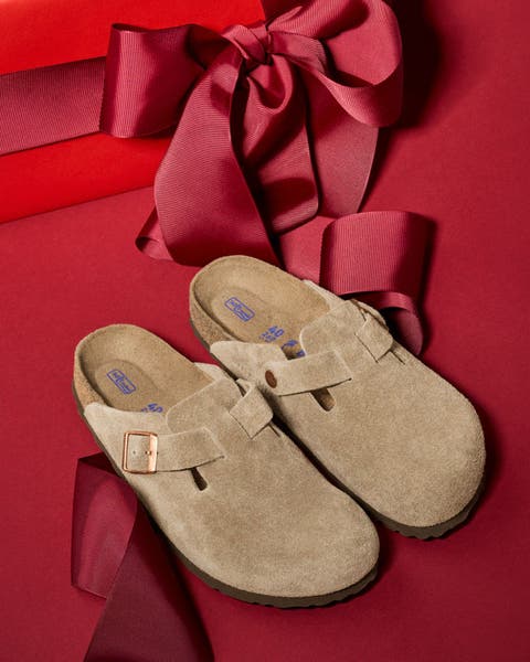 Taupe Birkenstock clogs sitting on a red bow with a red background