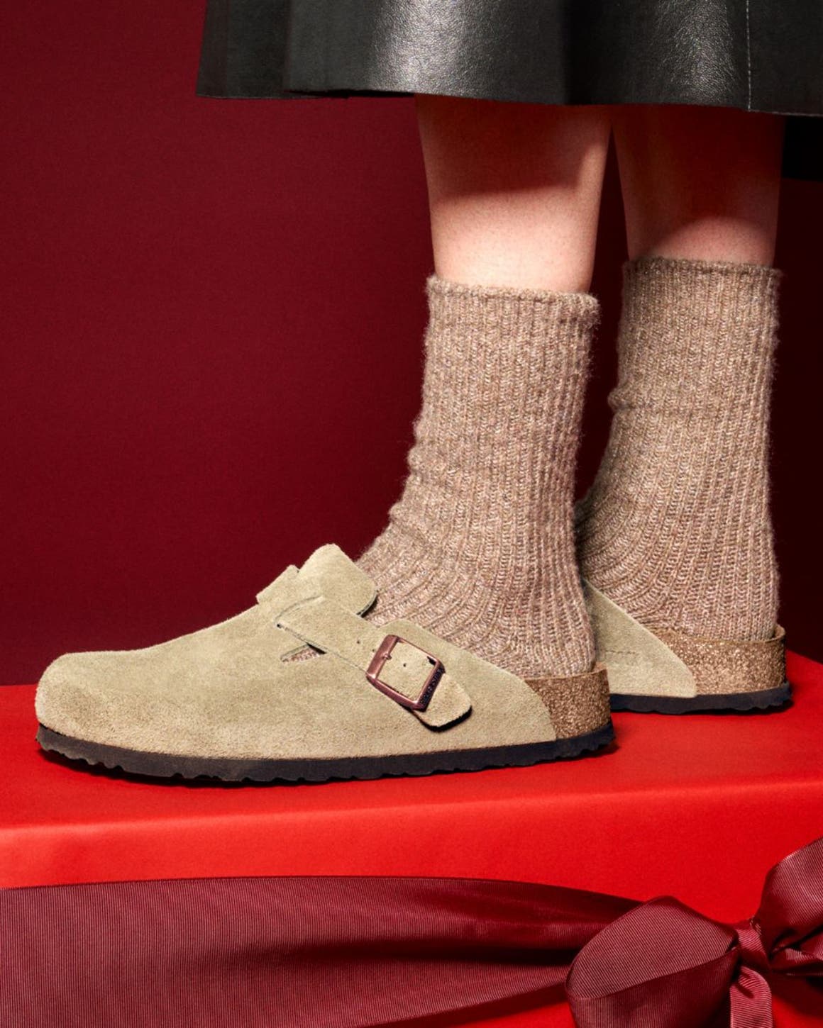 A person wearing Birkenstock clogs standing on a red gift box